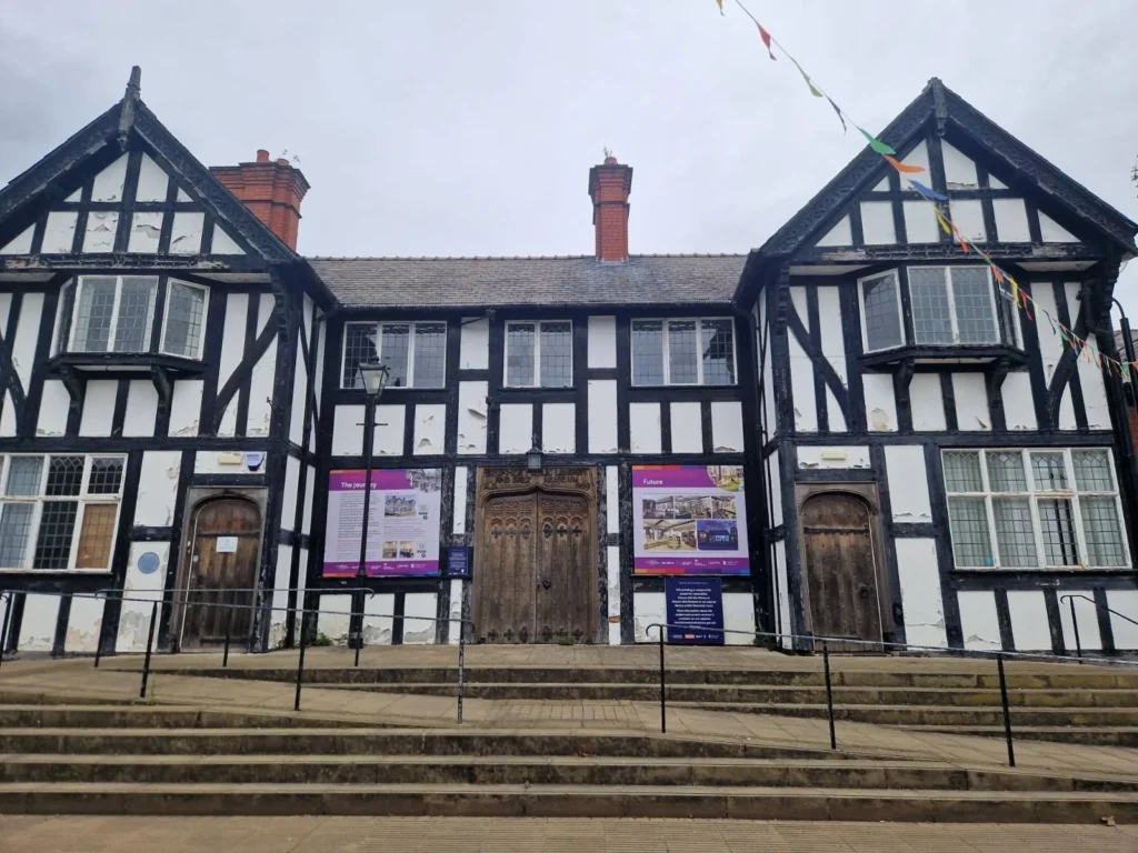 A historic half-timbered building with black beams, white walls, and large arched wooden doors.
