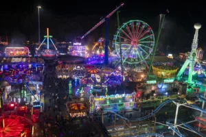 Aerial view of a vibrant night carnival with a lit Ferris wheel and colorful amusement park rides.