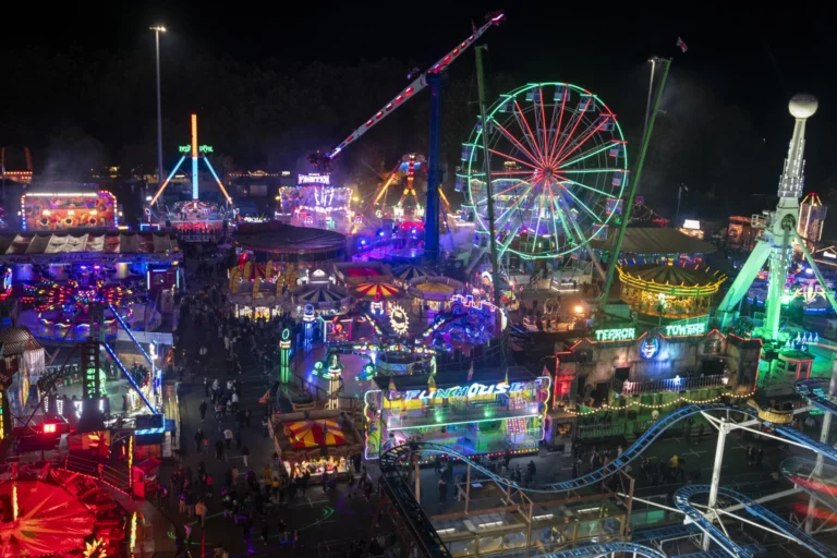 Aerial view of a vibrant night carnival with a lit Ferris wheel and colorful amusement park rides.