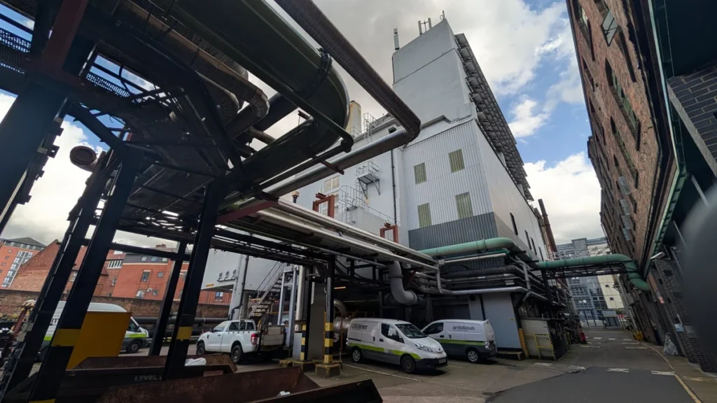 Low angle view of industrial pipes and white commercial vans parked by a factory.