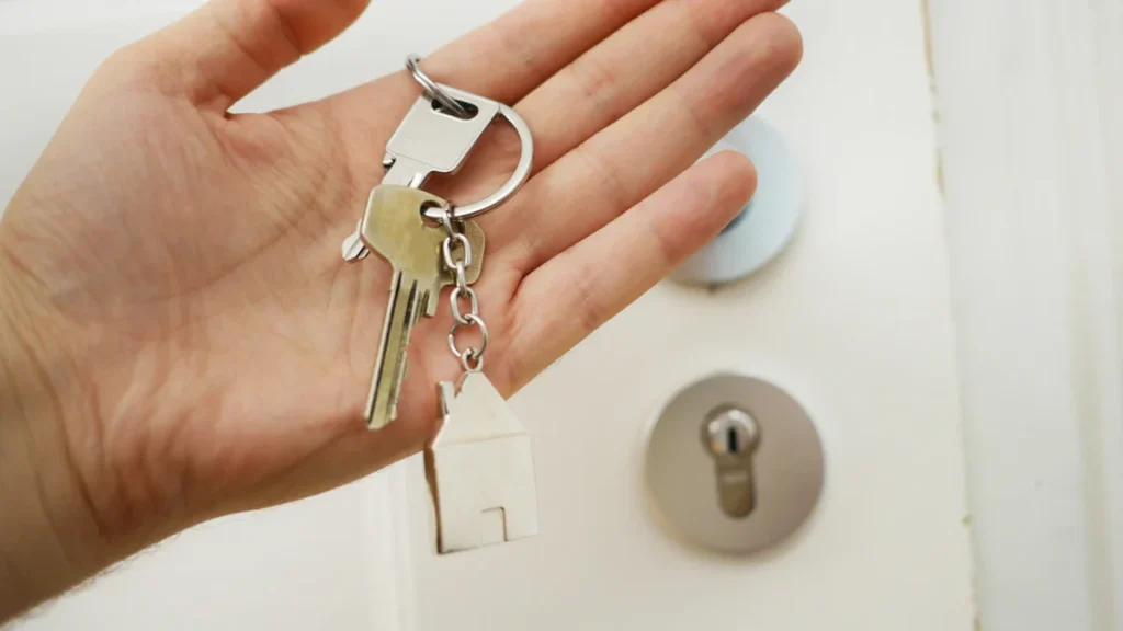 A person's hand holding a set of keys with a house-shaped metal keychain.