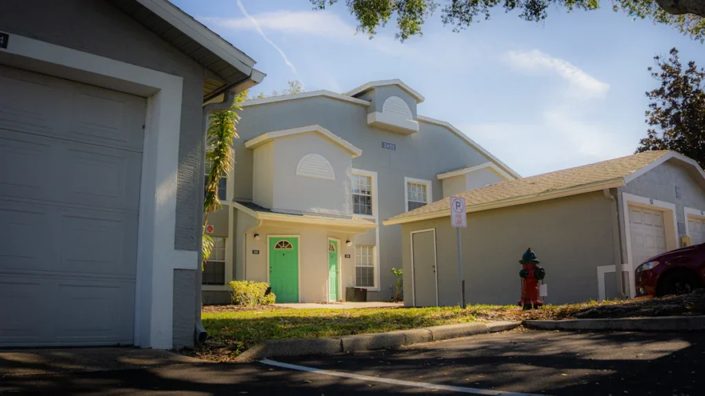 A residential apartment building featuring bright green doors situated next to several single-story garage units.