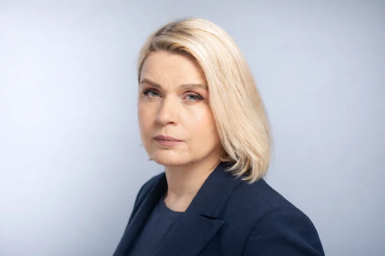 Headshot of a blonde woman wearing a dark blue blazer against a light gray background.