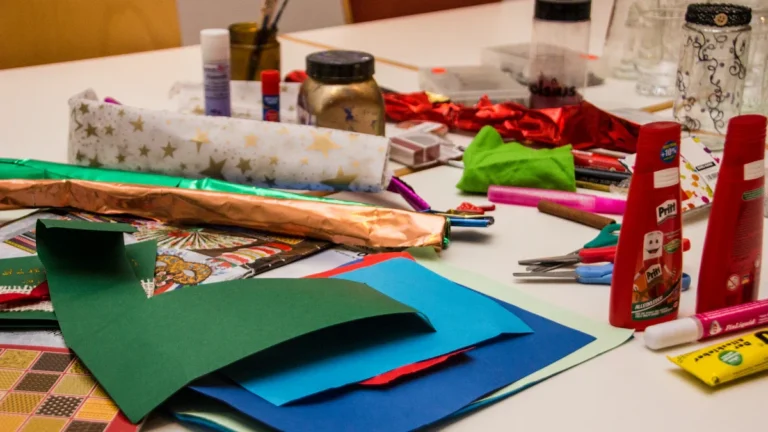 A table covered in colorful craft supplies including paper, glue sticks, and scissors for children's activities.