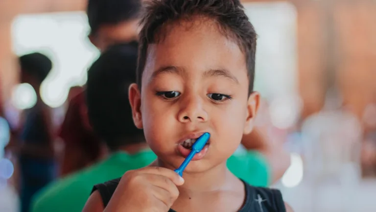 A young child focused on brushing their teeth with a blue toothbrush during a session.