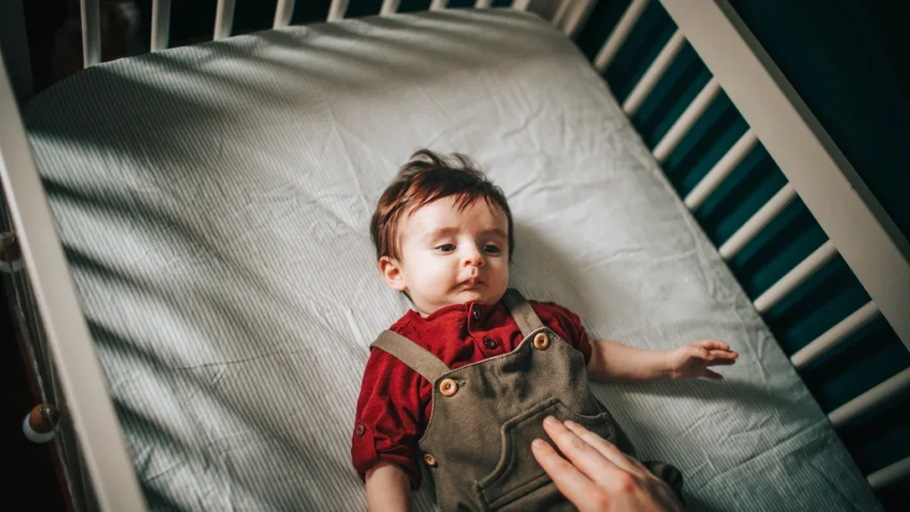 A close-up, top-down view of a baby lying in a cot as a parent's hand reaches in to check on them.