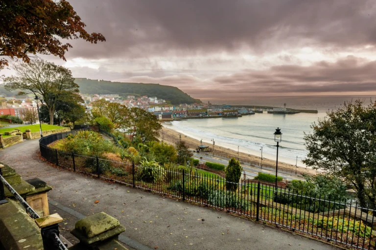 Elevated view of a coastal town harbor and sandy beach under a moody, overcast evening sky.
