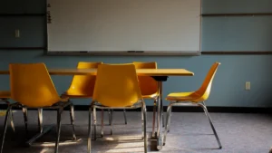 An empty school classroom featuring yellow chairs around a wooden table and a large white whiteboard.