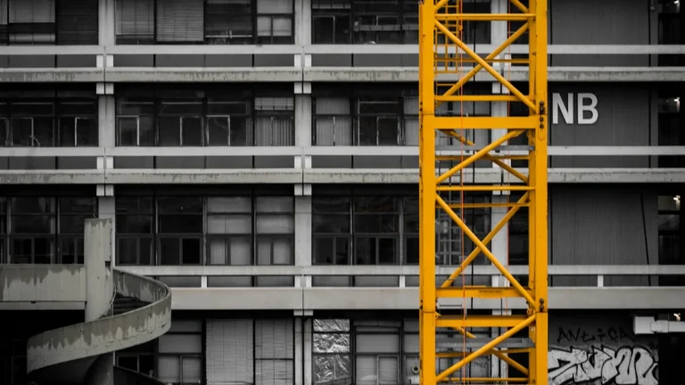 A yellow construction crane stands against a multi-story building facade, symbolizing urban development and growth.
