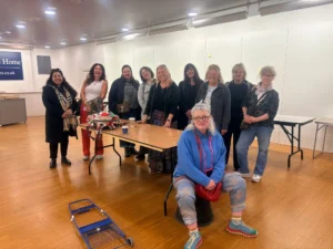 A group of ten women posing together in an indoor space with a folding table.
