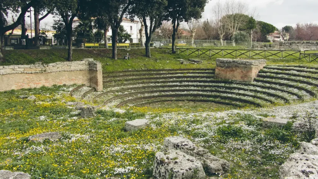 Ancient stone structure of the Ekklesiasterion in a lush green field in Italy