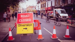 A red road closed sign and a yellow diversion sign on a busy British city street.