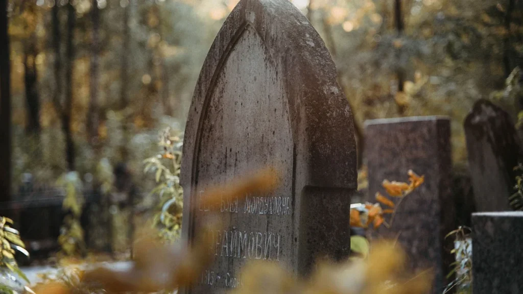 Close-up of an aged stone headstone in a wooded cemetery with soft autumn lighting.