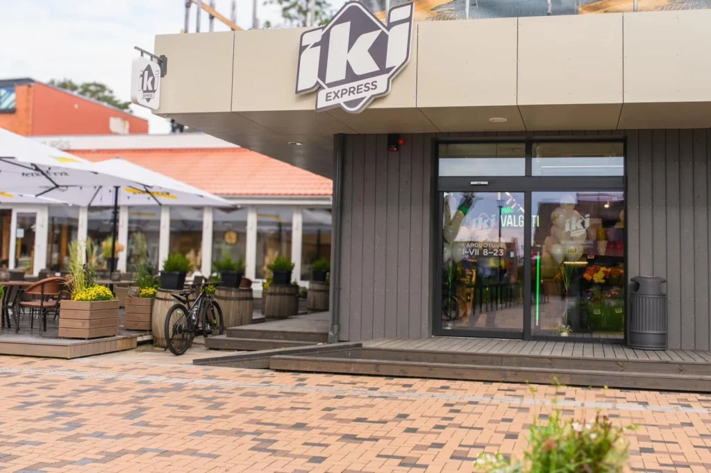 Front of an Iki Express grocery store with a black bicycle parked near cafe tables.