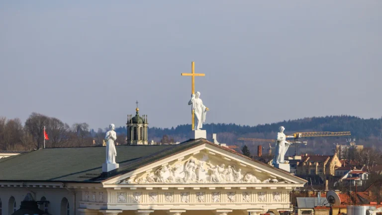 Statues of saints stand atop the neoclassical Vilnius Cathedral pediment under a clear blue sky.