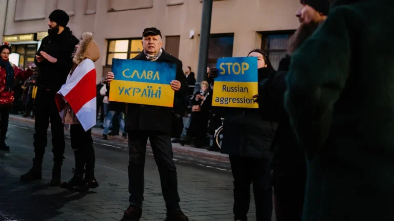 A man draped in the Lithuanian flag walks with a crowd carrying a large banner through Vilnius at night.