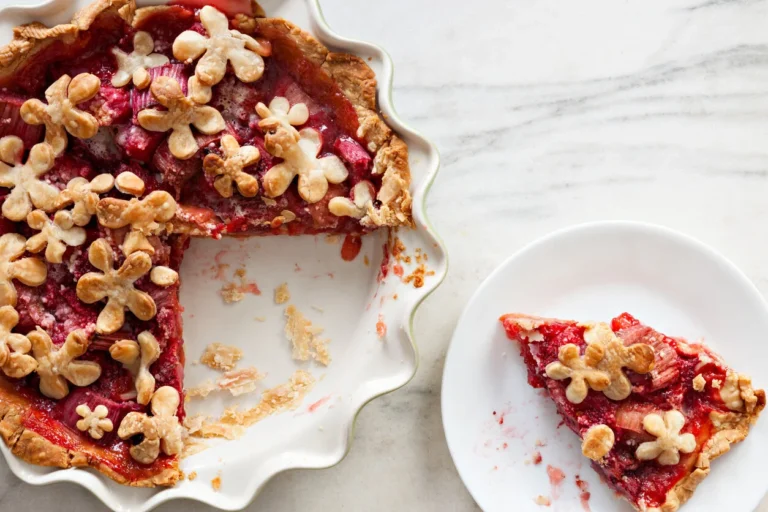 A red fruit pie topped with flower-shaped pastry cutouts in a scalloped ceramic baking dish.