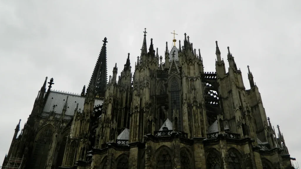A dramatic, low-angle view of a grand cathedral's Gothic spires against a grey, overcast sky.