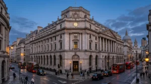 Neoclassical stone building in London with red buses and black taxis during evening twilight.