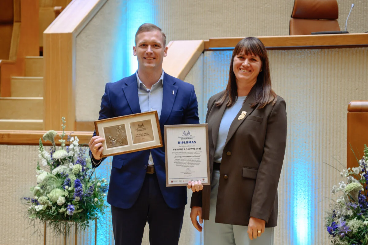A man and woman smiling while holding a framed plaque and a formal award certificate.