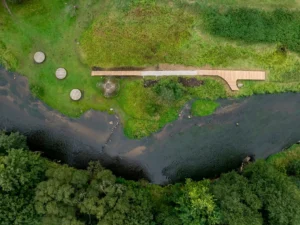 High-angle view of a wooden boardwalk and circular platforms along a lush green riverbank.