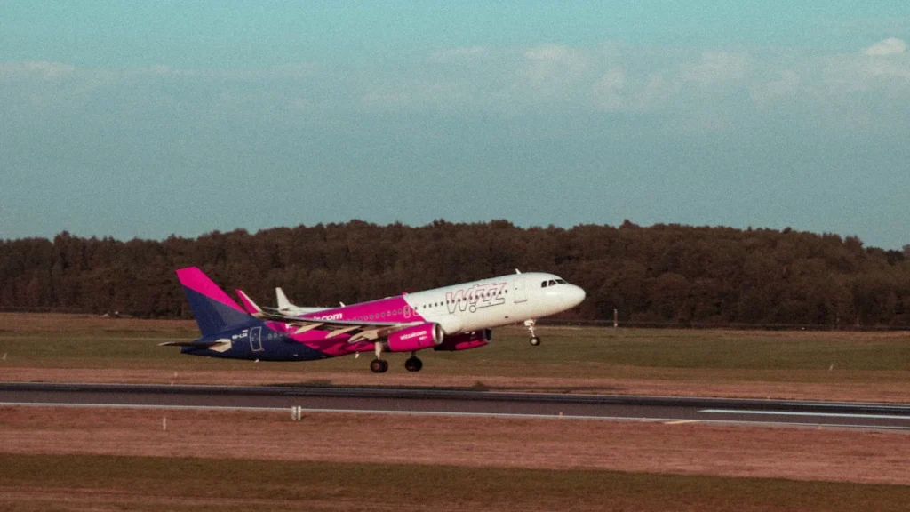 A Wizz Air passenger jet taking off from the runway at Vilnius Airport against a clear sky.