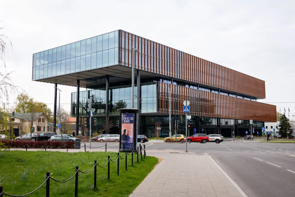 A modern glass building featuring a large cantilevered upper floor with vertical orange decorative slats.