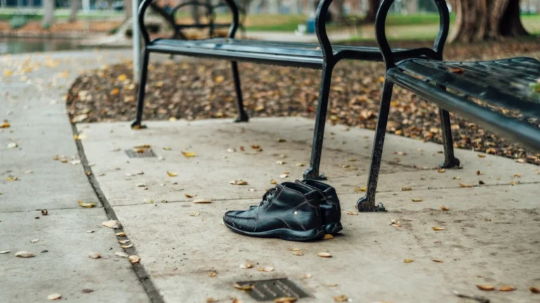 A pair of black leather shoes left alone on a concrete path near empty park benches.