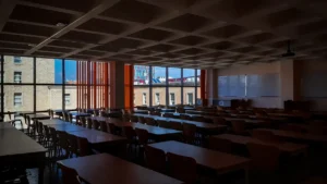 An expansive school lecture hall with rows of wooden desks under a modern waffle-slab ceiling.