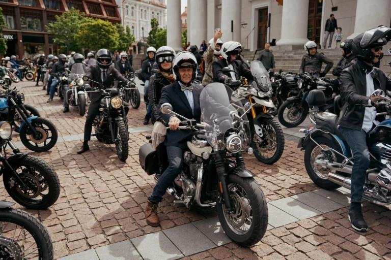 A crowd of elegantly dressed motorcyclists on a cobblestone street in front of classic architecture.