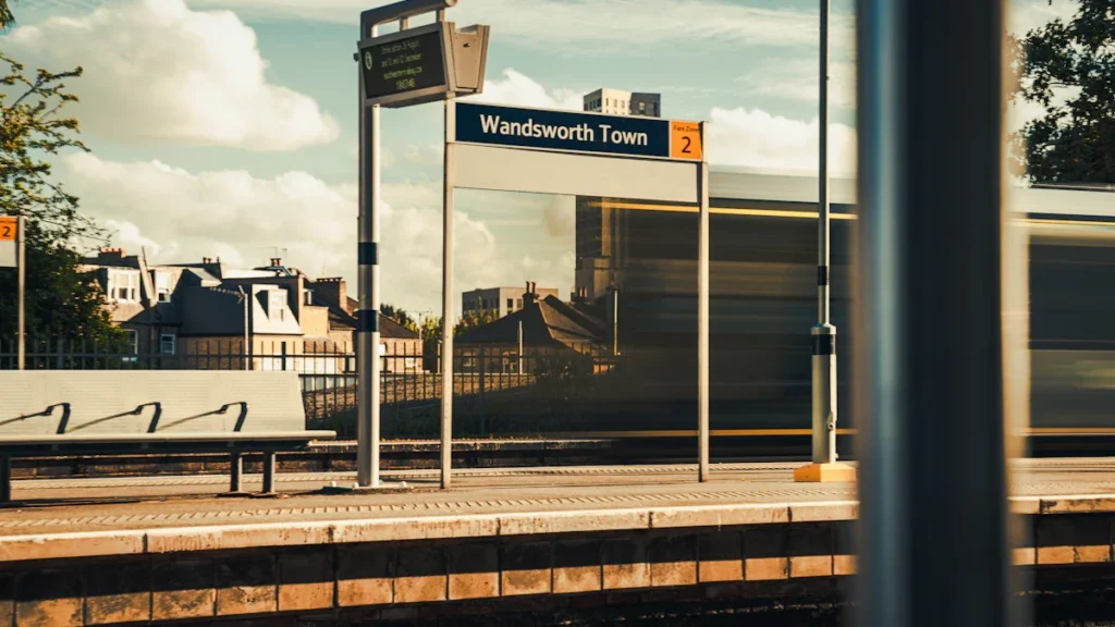A train passing through the Wandsworth Town station platform under a clear sky in London.