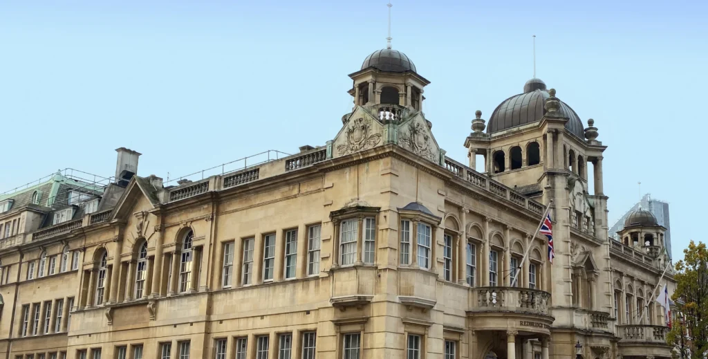 Ornate light-colored stone building featuring architectural domes, sash windows, and a Union Jack flag.