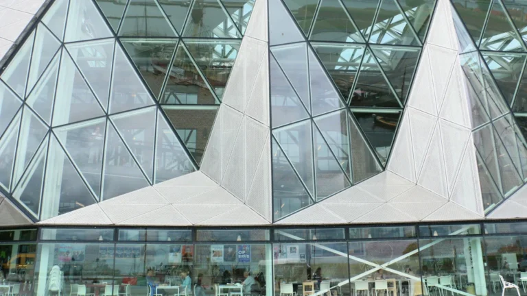 A modern building featuring a geometric glass facade and a community cafe visible through the windows.