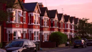A row of red brick Victorian terraced houses in London under a dusky pink sunset sky.