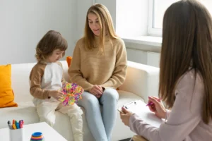 Young boy plays with a colorful toy while his mother sits beside a consulting professional.