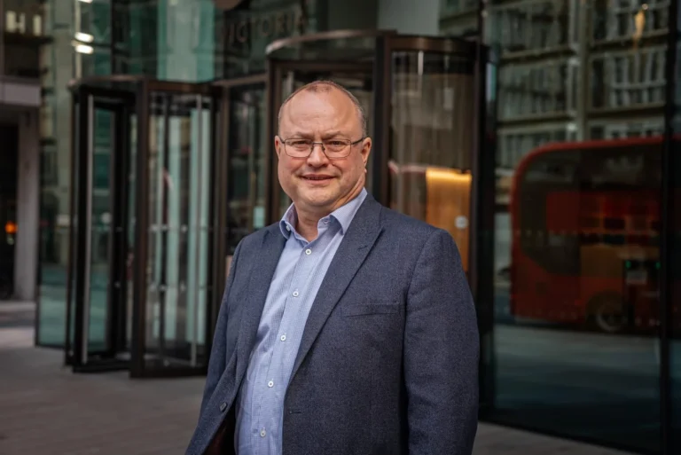 A man with glasses wearing a blue blazer and light blue shirt outside a glass building.