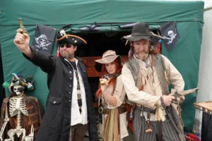 Three people in pirate costumes pose with replica pistols in front of a green tent.