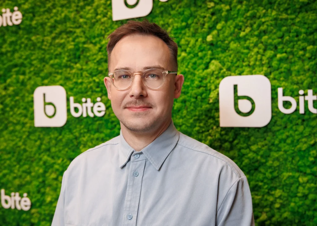 Man with glasses and light blue shirt standing against a green wall with bitė logos.
