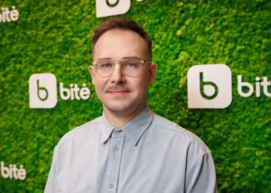 Man with glasses and light blue shirt standing against a green wall with bitė logos.