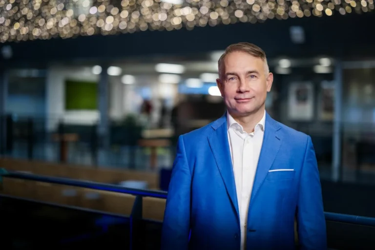 A professional man in a bright blue blazer and white shirt stands in a modern office.