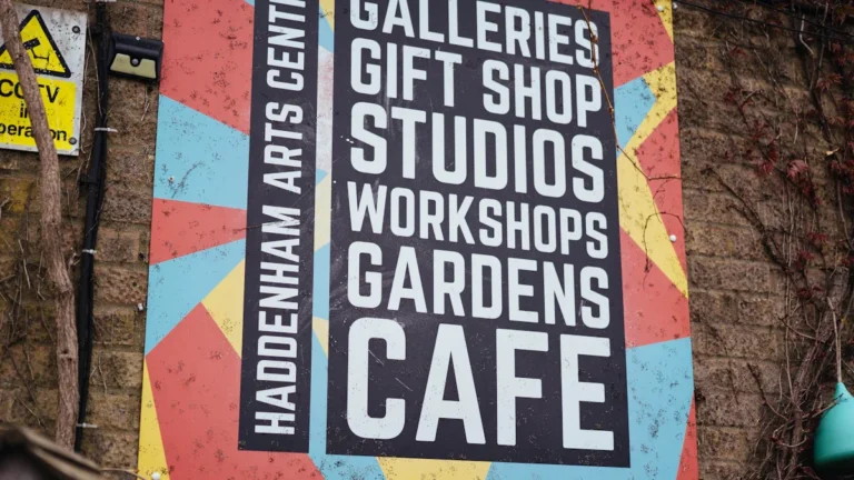 A colorful sign for a UK arts centre listing facilities like studios, workshops, and community gardens.