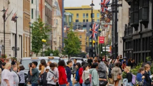 A large crowd of people, including many young adults, crossing a busy city street in the United Kingdom.