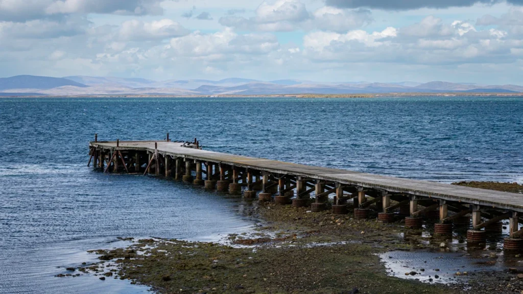 A long wooden pier stretching into the waters near West Falkland, UK territory.