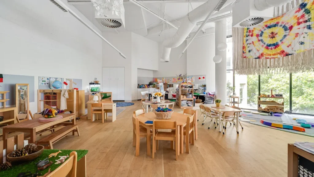 Modern open-plan classroom featuring wooden furniture and large windows overlooking lush greenery.