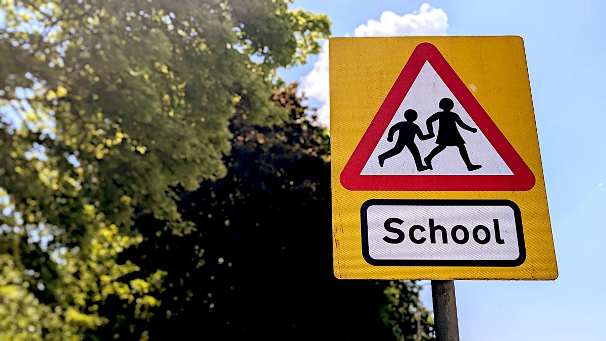 Classic British yellow school crossing warning sign with children silhouettes against a blue sky.