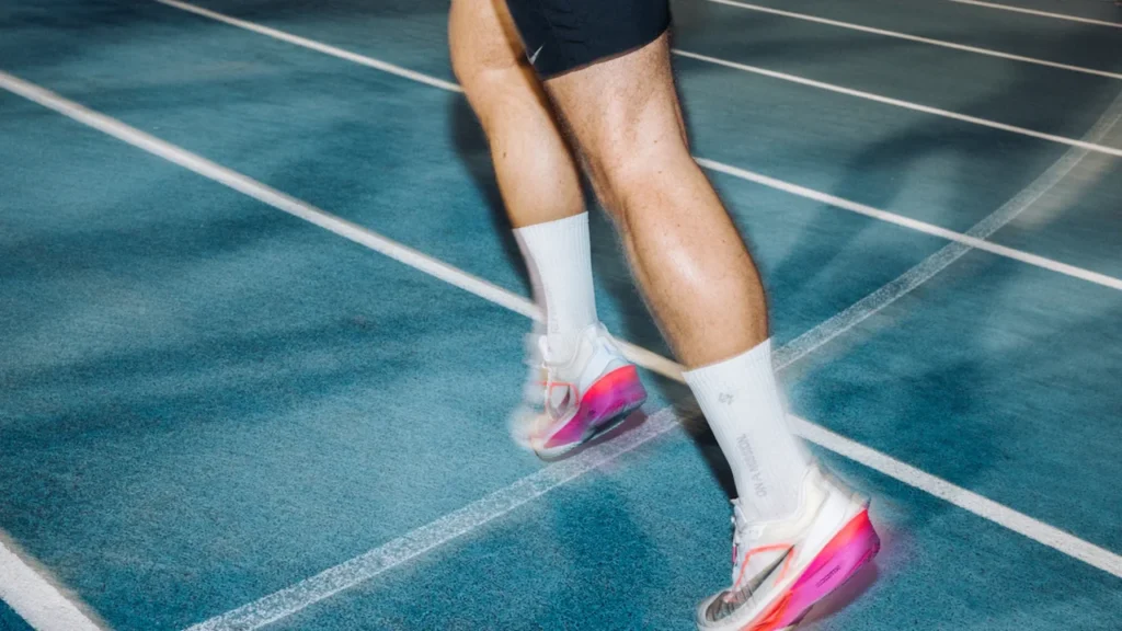 Close up of an athlete's legs and running shoes on a blue track.