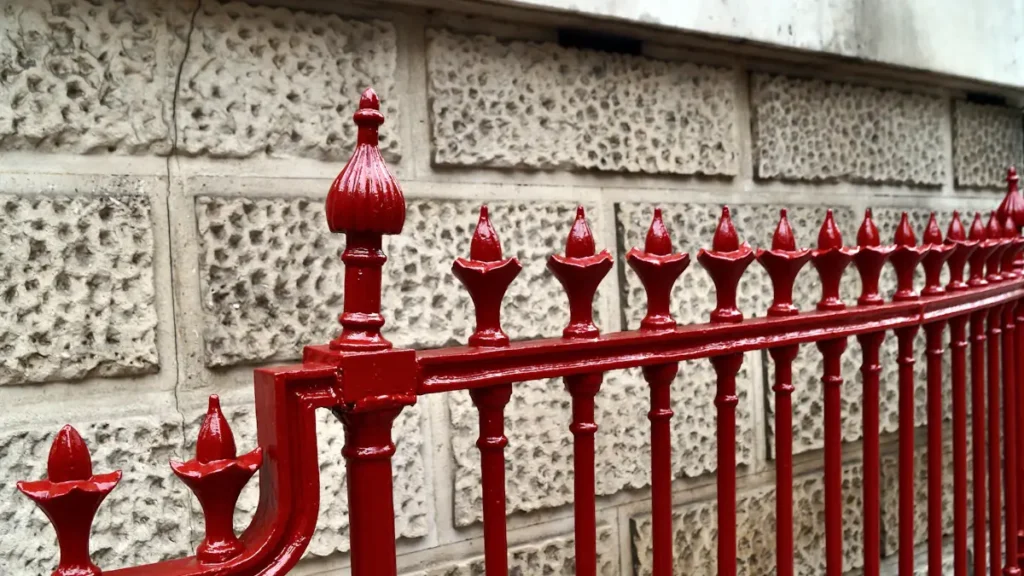 Close-up of newly painted red iron railings against a textured stone wall.