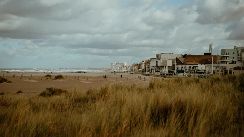 Expansive sandy beach with grassy dunes under a dramatic, moody, overcast British sky.