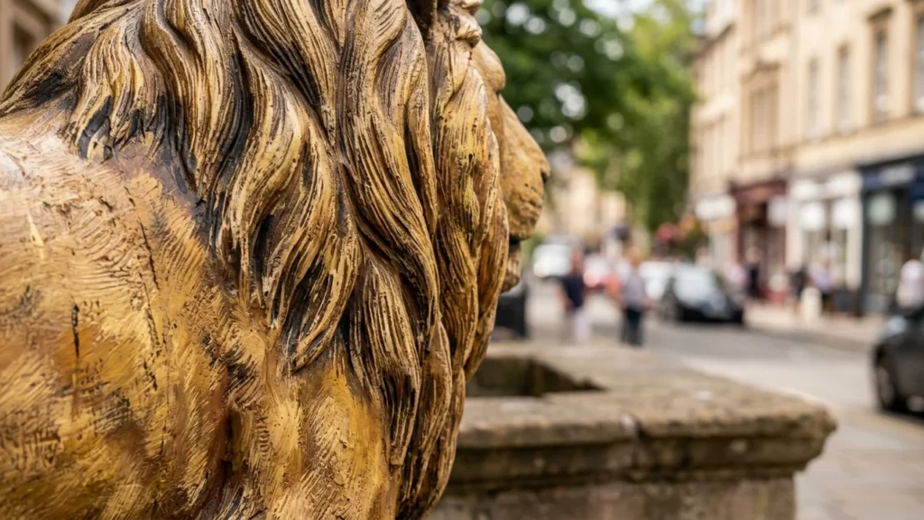 Close-up side view of a textured gold lion statue on a blurry street.