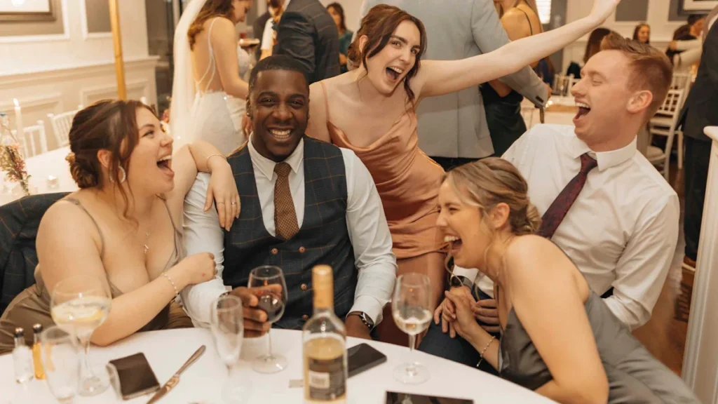 Group of friends laughing and celebrating together at a wedding dinner table.